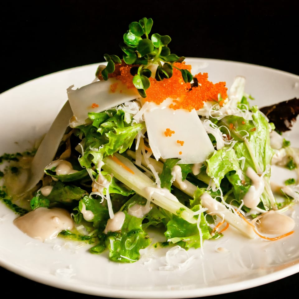 Fresh green salad with white fish, orange tobiko, and microgreens, drizzled with dressing.