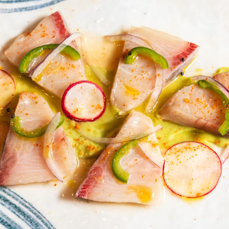 Kakui Sushi's hamachi sashimi with green peppers, radishes, and a light sauce on a white plate.