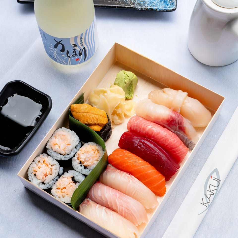 Kakui Sushi bento box with various nigiri, maki, uni, wasabi, ginger, and a sake bottle.