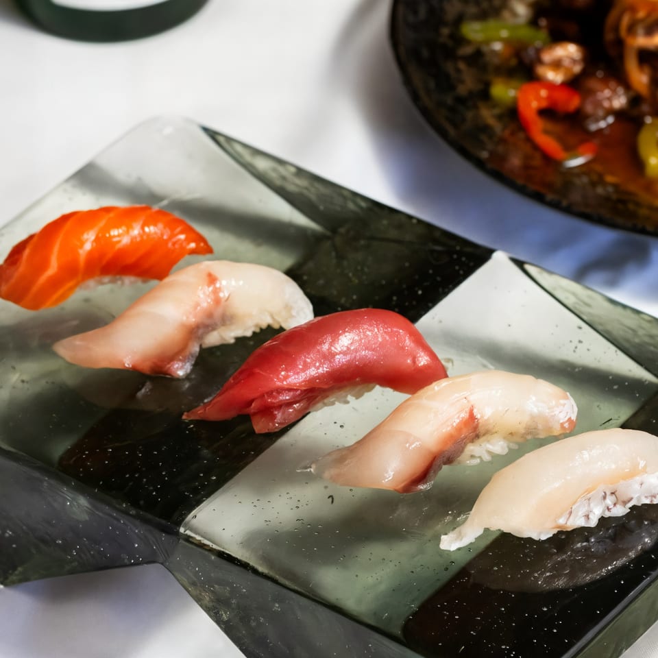Five pieces of Kakui Sushi nigiri, including salmon, tuna, and white fish, on a checkered plate.