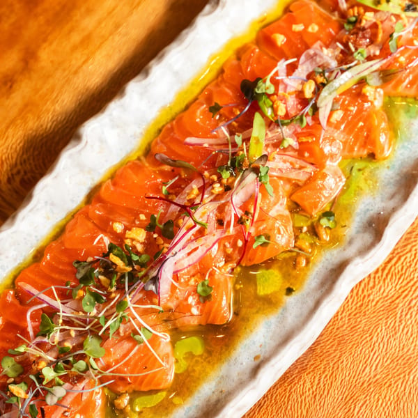 Kakui Sushi's salmon carpaccio with microgreens, red onion, and a vibrant yellow sauce.