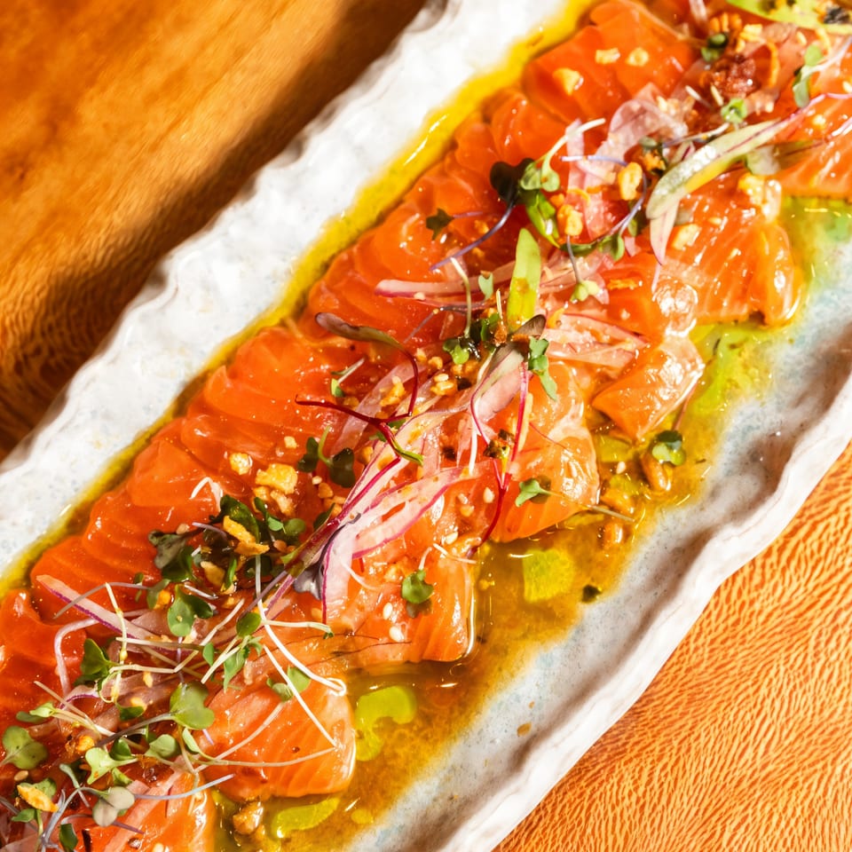 Kakui Sushi's salmon carpaccio with microgreens, red onion, and a vibrant yellow sauce.